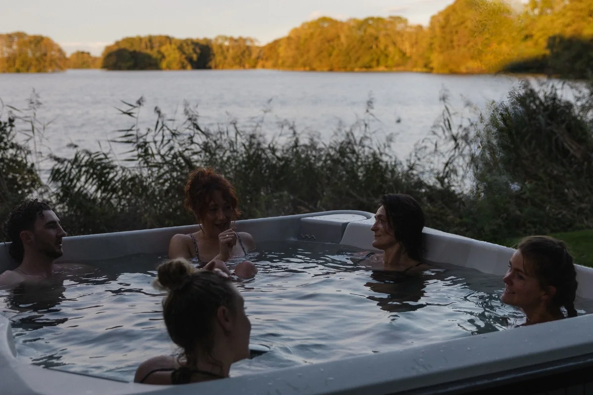 Fünf Gäste im Sprudelbad des RAUS. im Gespräch, dahinter Schilf und der Bistensee in der Abendsonne