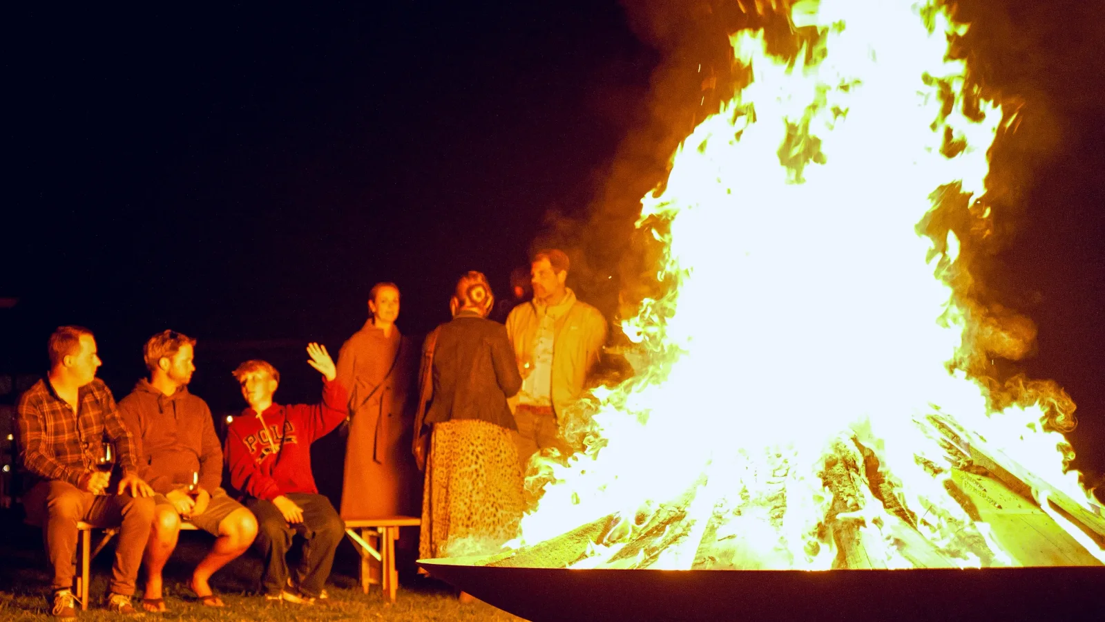 Gäste am großen Feuer in der Feuerschale auf der Seewiese bei Nacht