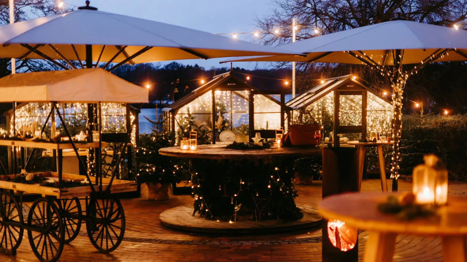 Weihnachtsmarkt am See: beleuchtete Glashäuser, Lichterketten und Kerzen auf der Seeterrasse in der blauen Stunde