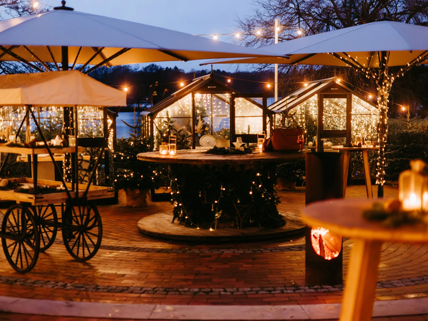 Julemarkt zur blauen Stunde auf der Seeterrasse am Bistensee mit beleuchteten Glashäuschen und Lichterketten