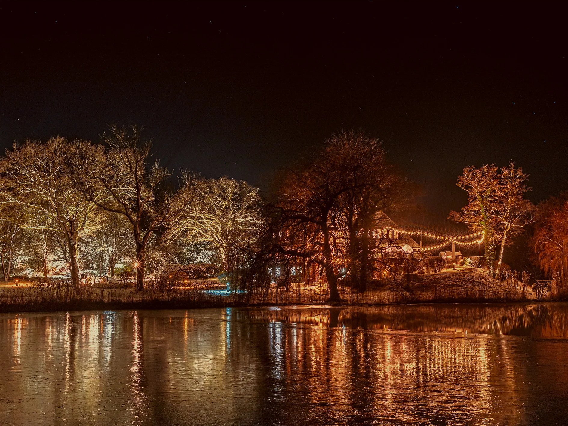 Seehotel Töpferhaus am Bistensee in einer Winternacht mit Lichterketten und Spiegelungen auf dem See