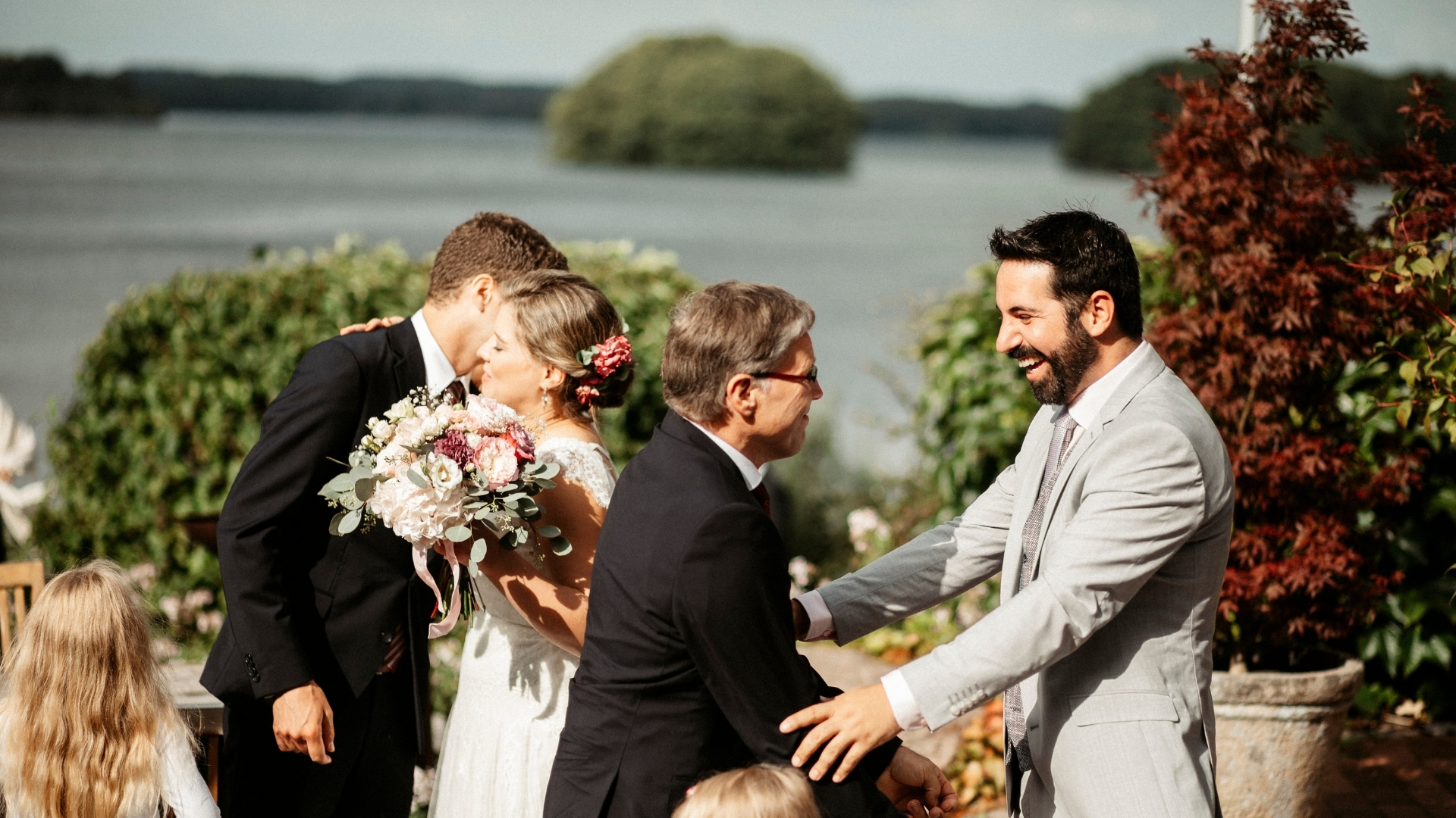 Brautpaar und Gäste beglückwünschen sich bei einer Hochzeit im Freien vor einem See - Seehotel Töpferhaus in Schleswig-Holstein